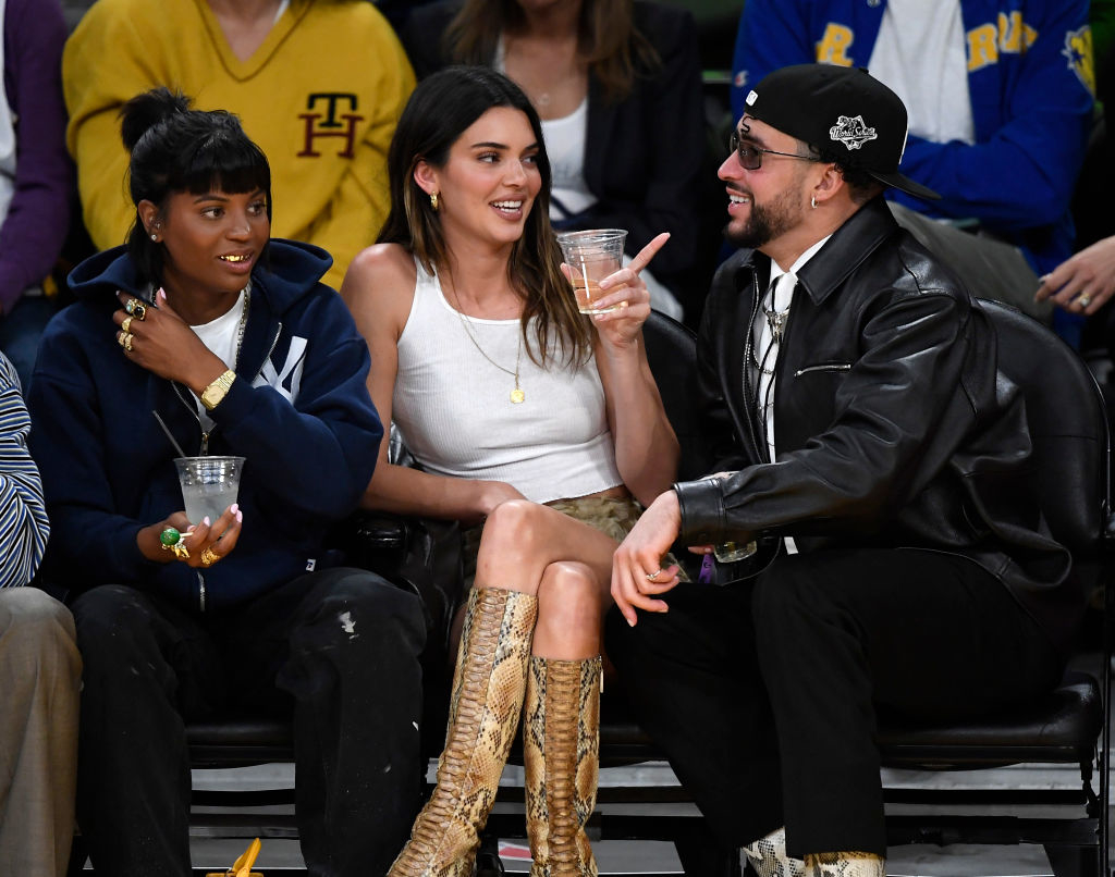Kendall holding a drink as she sits court side at a game next to Bad Bunny