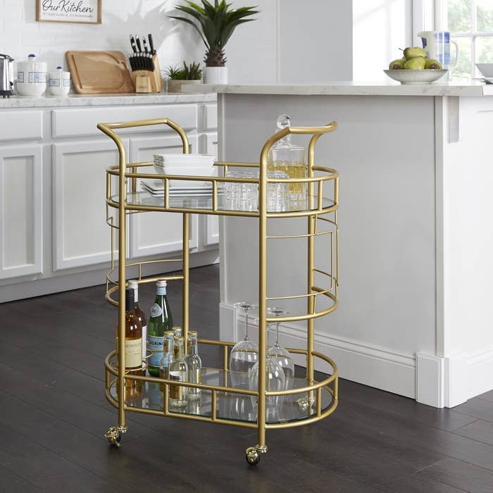 the bar cart with beverages and glasses on the bottom and dishes on the top shelf