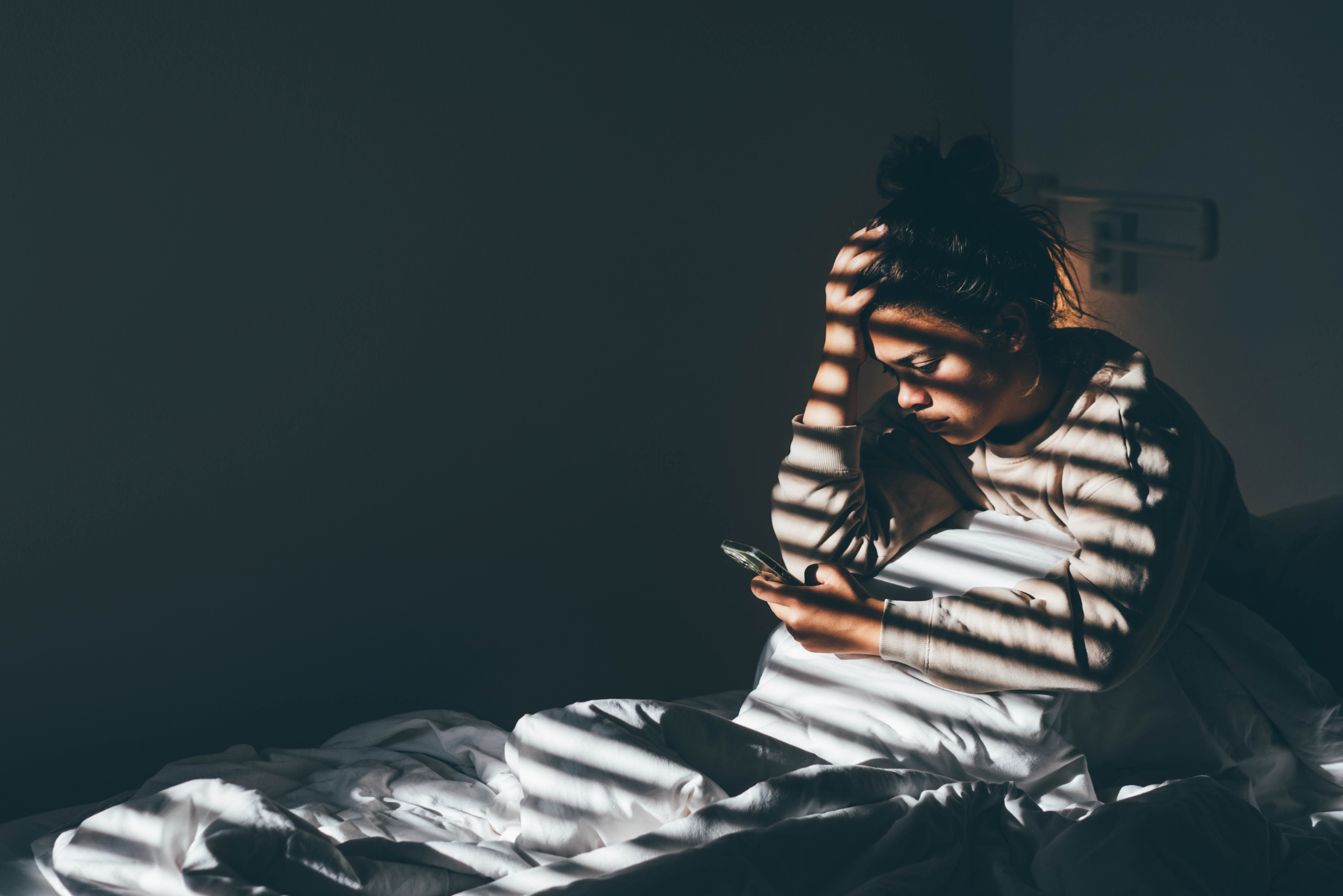 worried women sitting up in bed looking up symptoms on her phone
