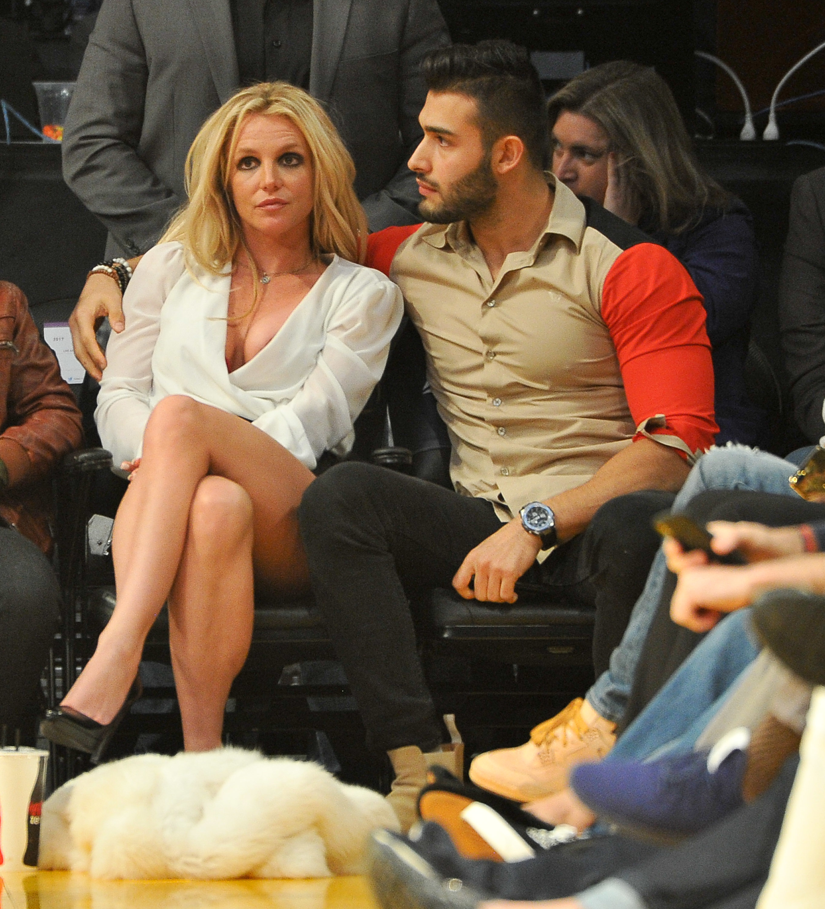 Britney Spears and Sam Asghari sitting court side at a basketball game. Sam has his arm around Britney&#x27;s shoulders