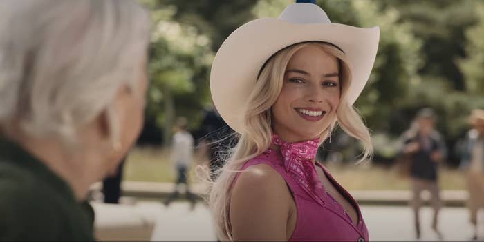 Margot Robbie as Barbie wearing a Cowboy-inspired outfit smiling and looking at another person in a scene from the film &quot;Barbie&quot;