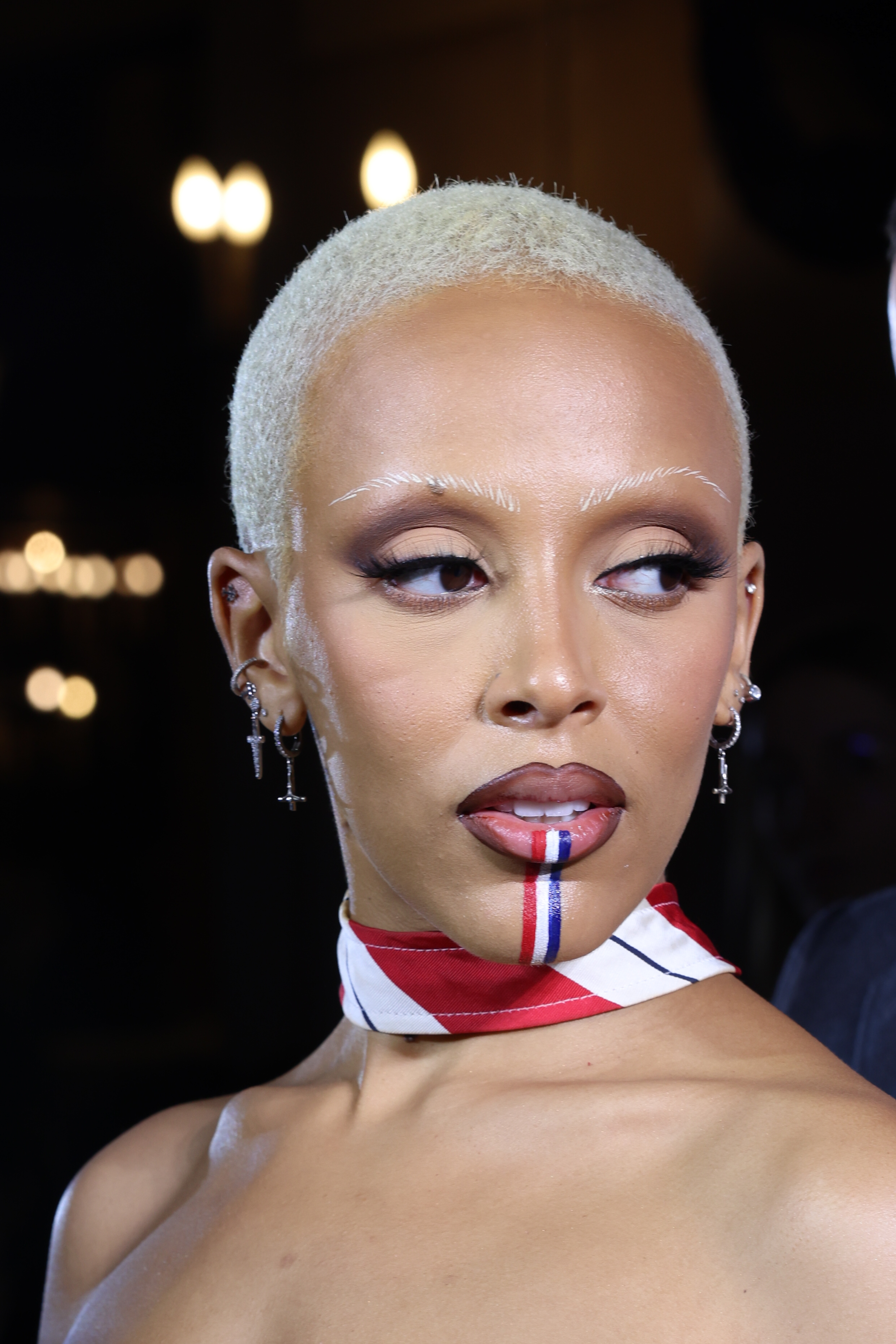 A close-up of Doja wearing a choker and red, white, and blue lip and chin makeup stripes