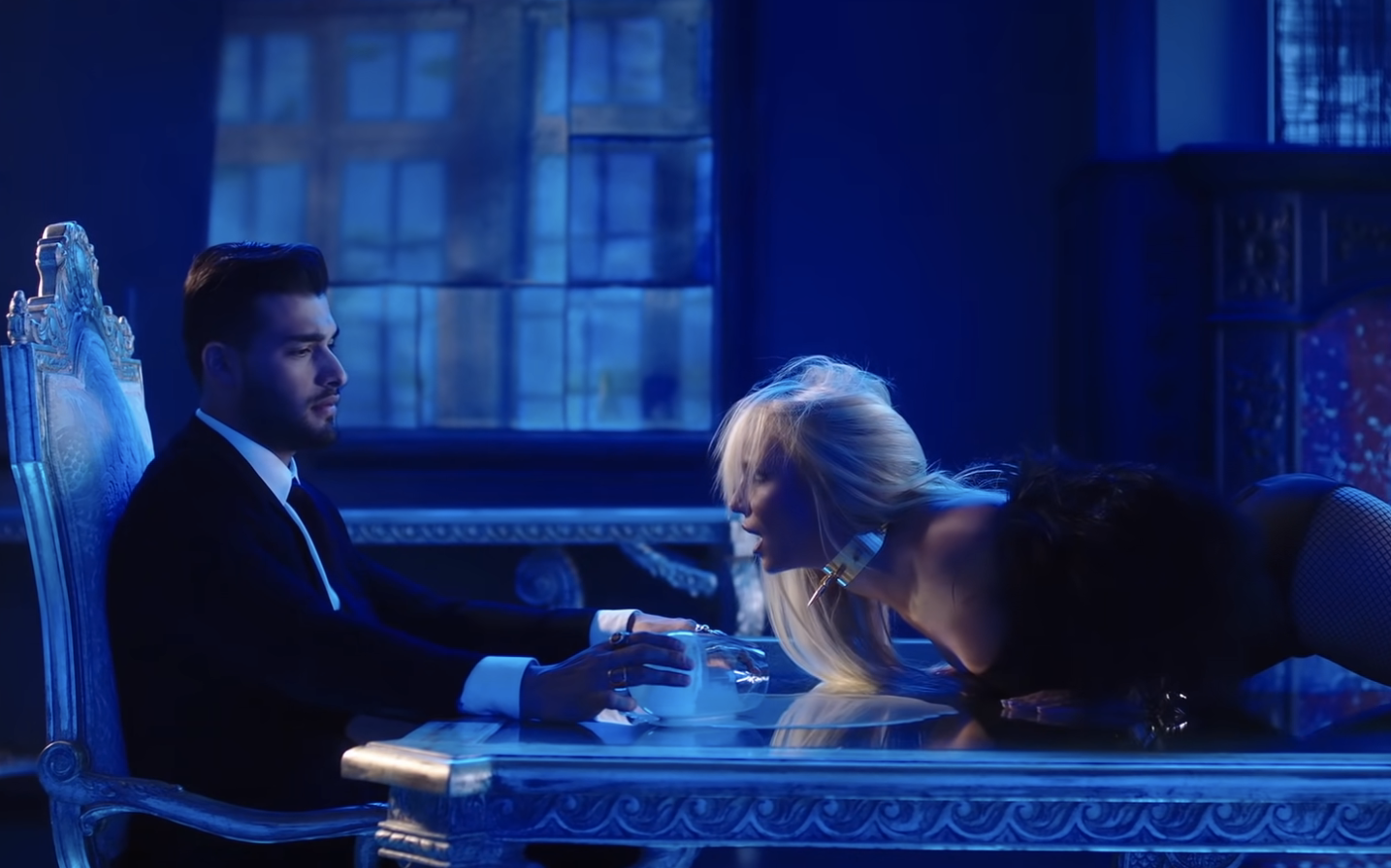 Screenshot from the &quot;Slumber Party&quot; video of Britney lying on a dining table in front of Sam
