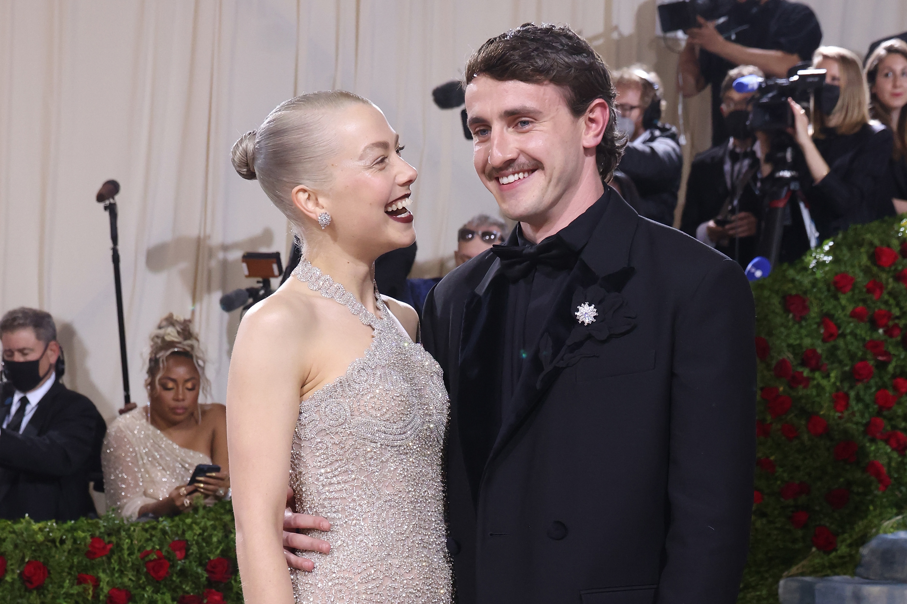 Close-up of Phoebe and Paul smiling at a media event with paparazzi in the background