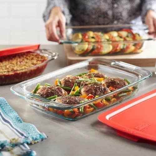 Glass baking dish with chicken and vegetables and red lid next to it