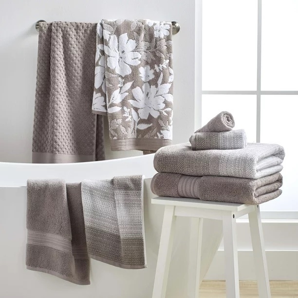 Beige towels hanging up by a tub and folded on a white stool