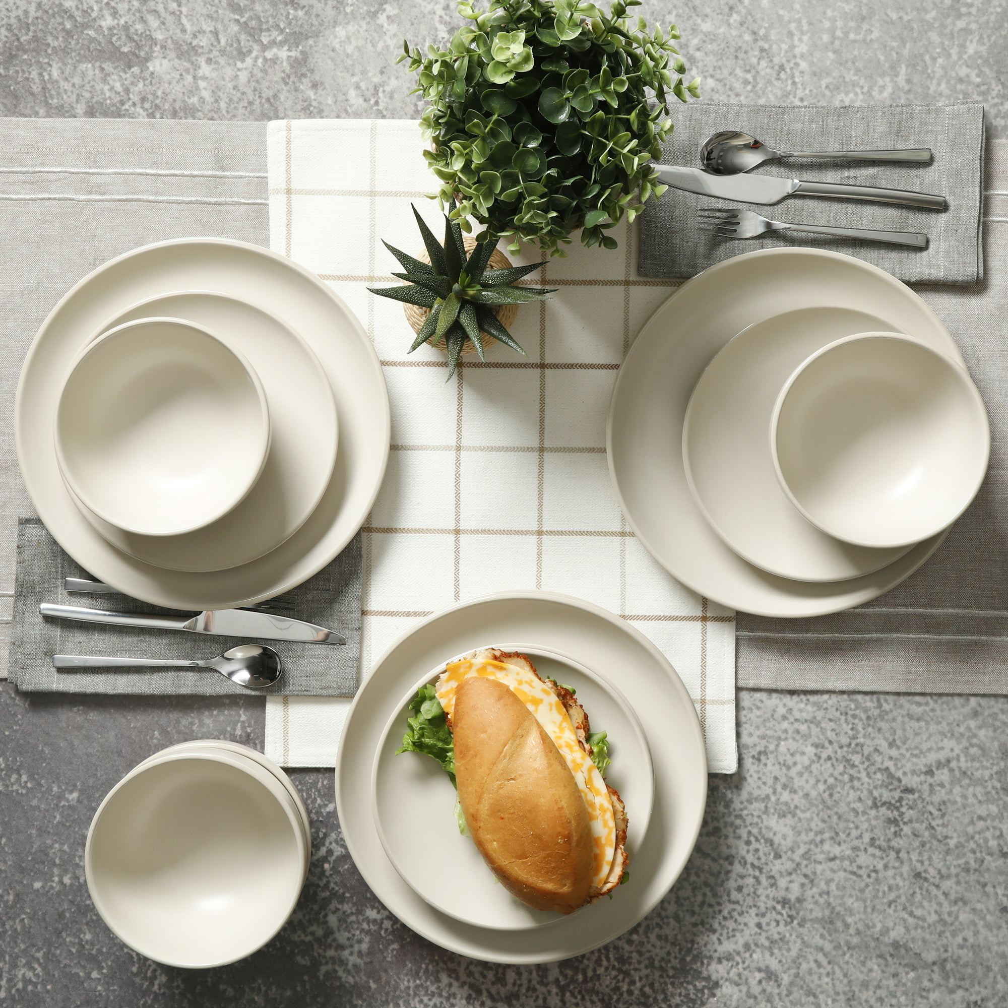 Beige dinnerware set on a table with a runner, silverware and sandwich