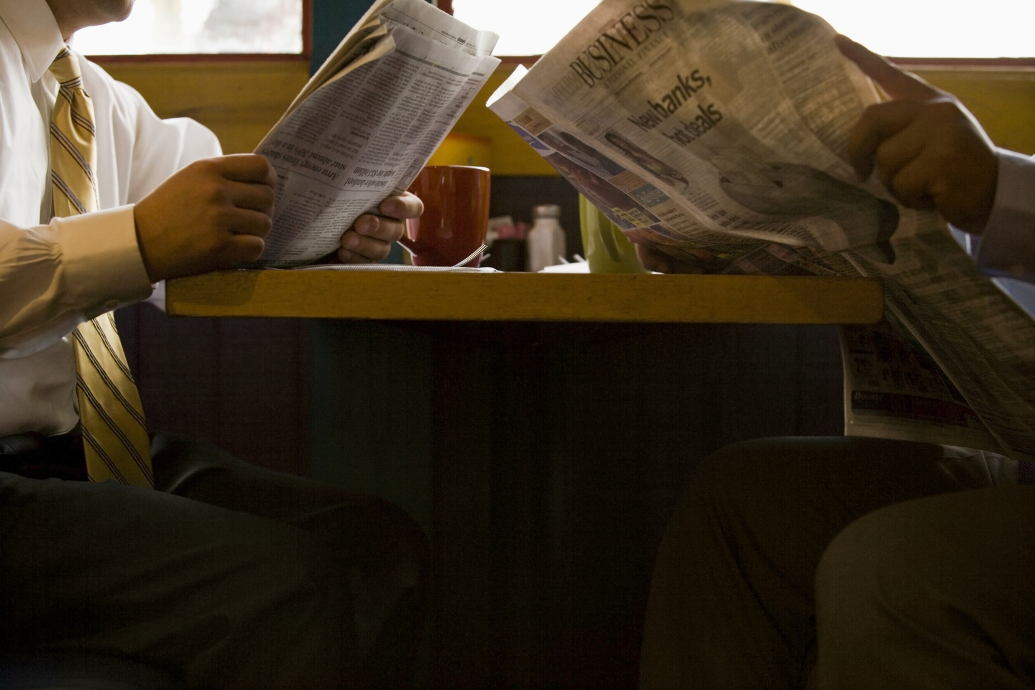 Two people are reading newspapers at a restaurant table
