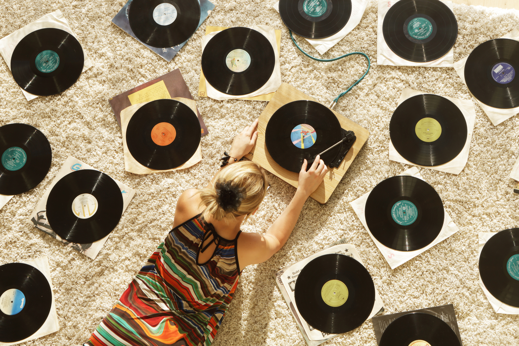 A young woman is on the floor surrounded by vinyls, playing a record player