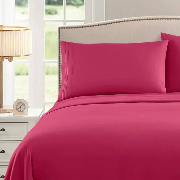 Hot pink sheets on an upholstered beige bed next to a white wooden nightstand