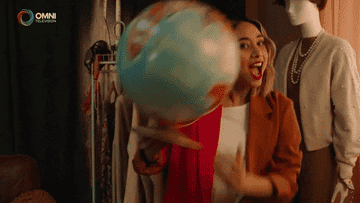 A woman spinning a globe and saying &quot;we&#x27;re going abroad!&quot;