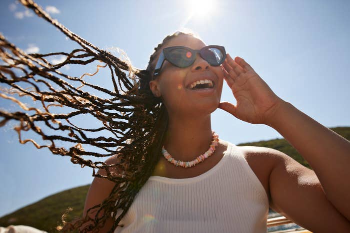 Happy young woman with tousled braided hair adjusting sunglasses during summer