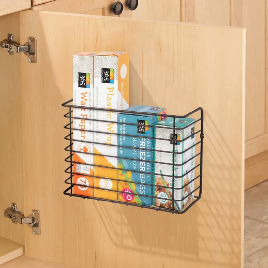 a wire rack holding plastic wrap and tinfoil mounted to the inside of a cabinet