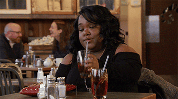Woman taking a sip of a drink at a restaurant and saying &quot;hot mess.&quot;