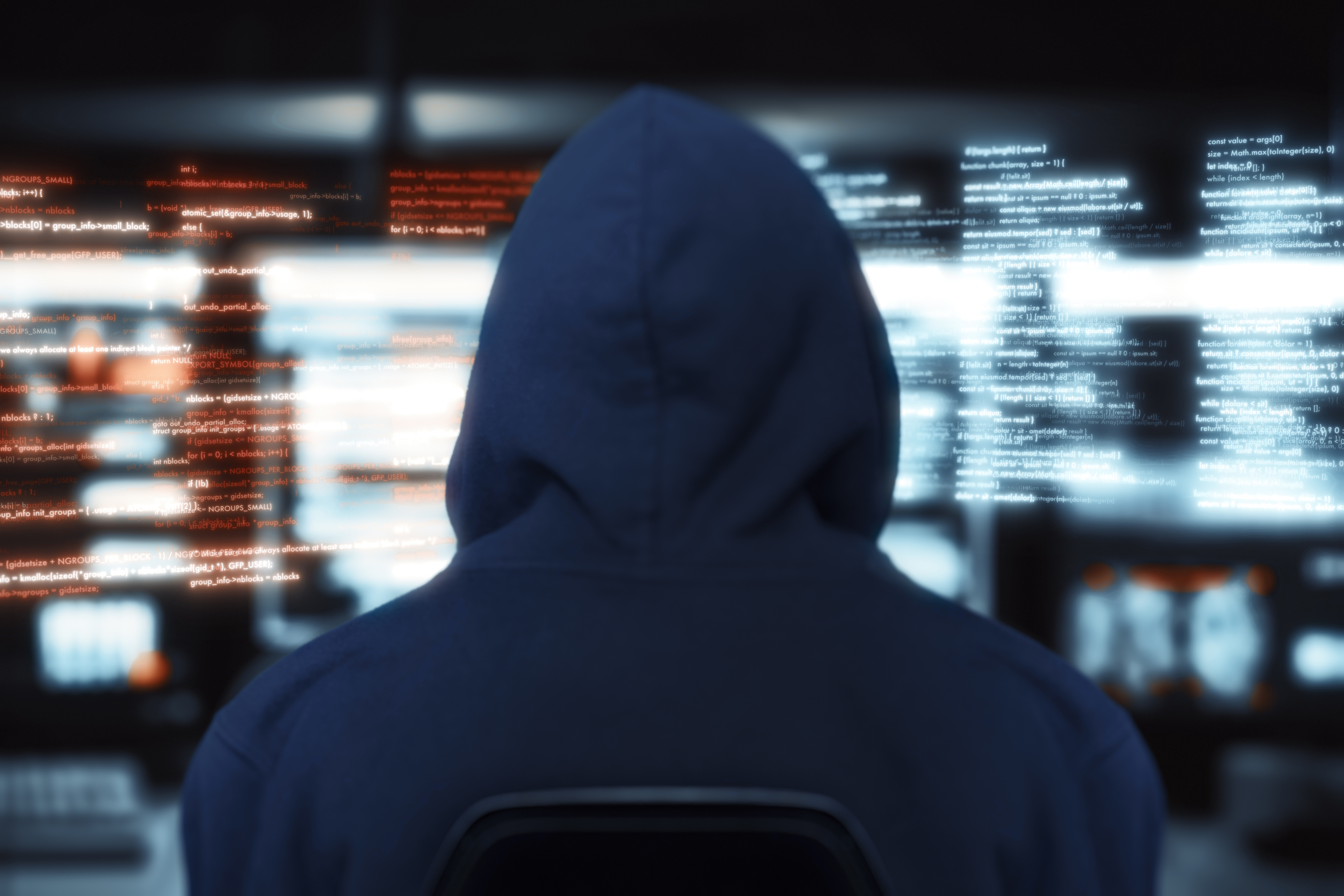 A hacker wearing a hoodie in front of multiple computer screens