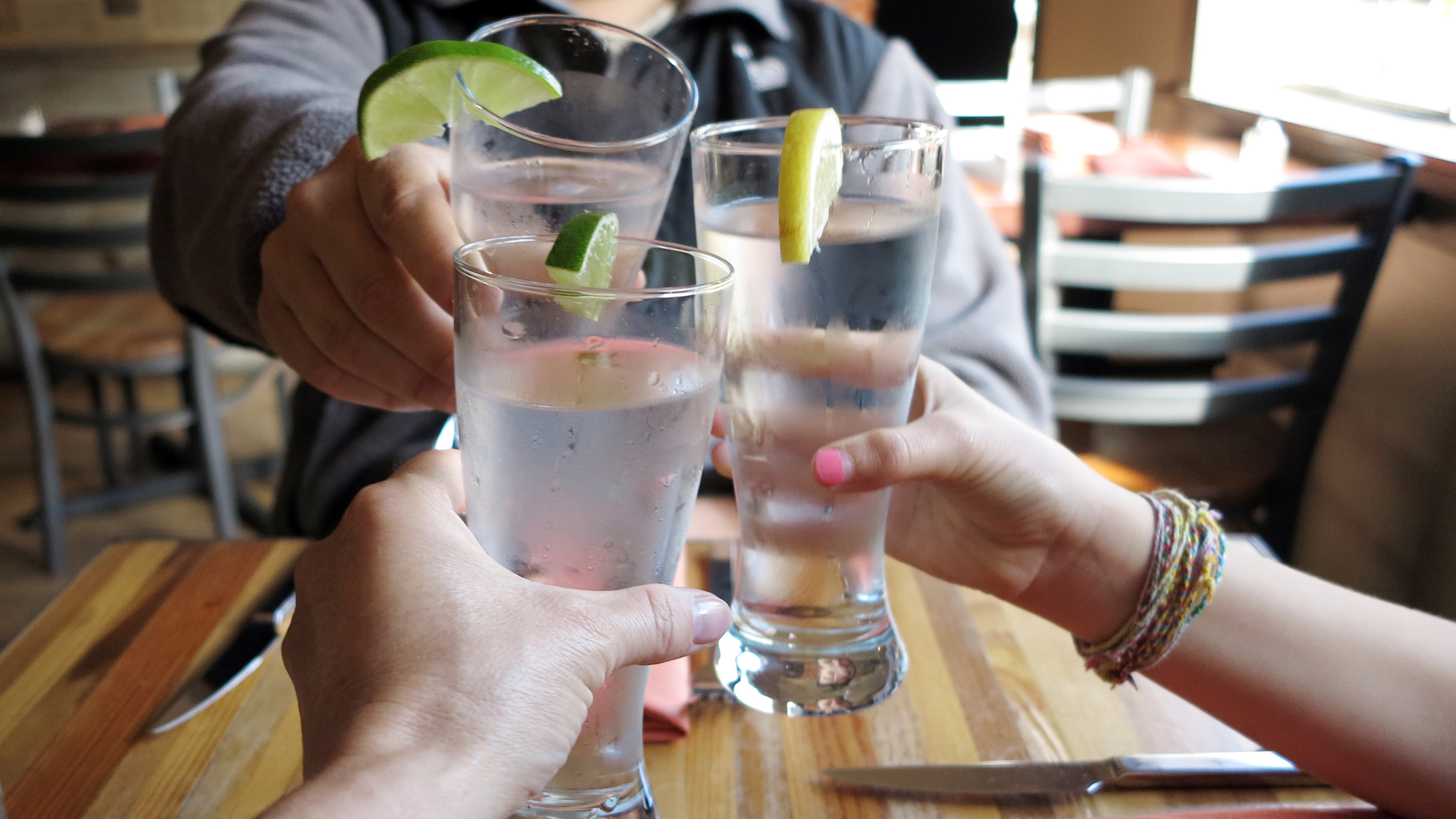 three diners cheers&#x27;ing their water glasses at a restaurant table