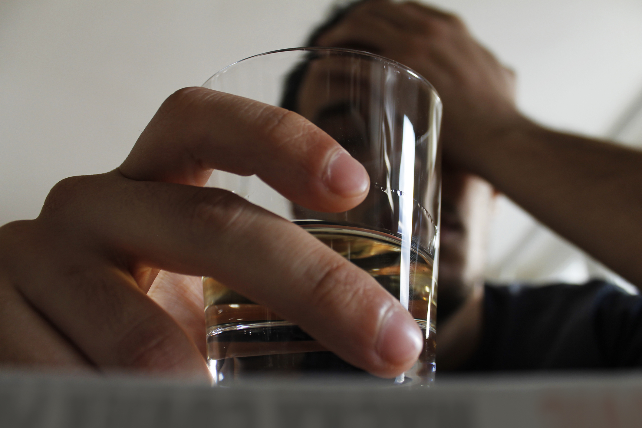 Close-up of a glass of liquor held by someone with their hand on their face