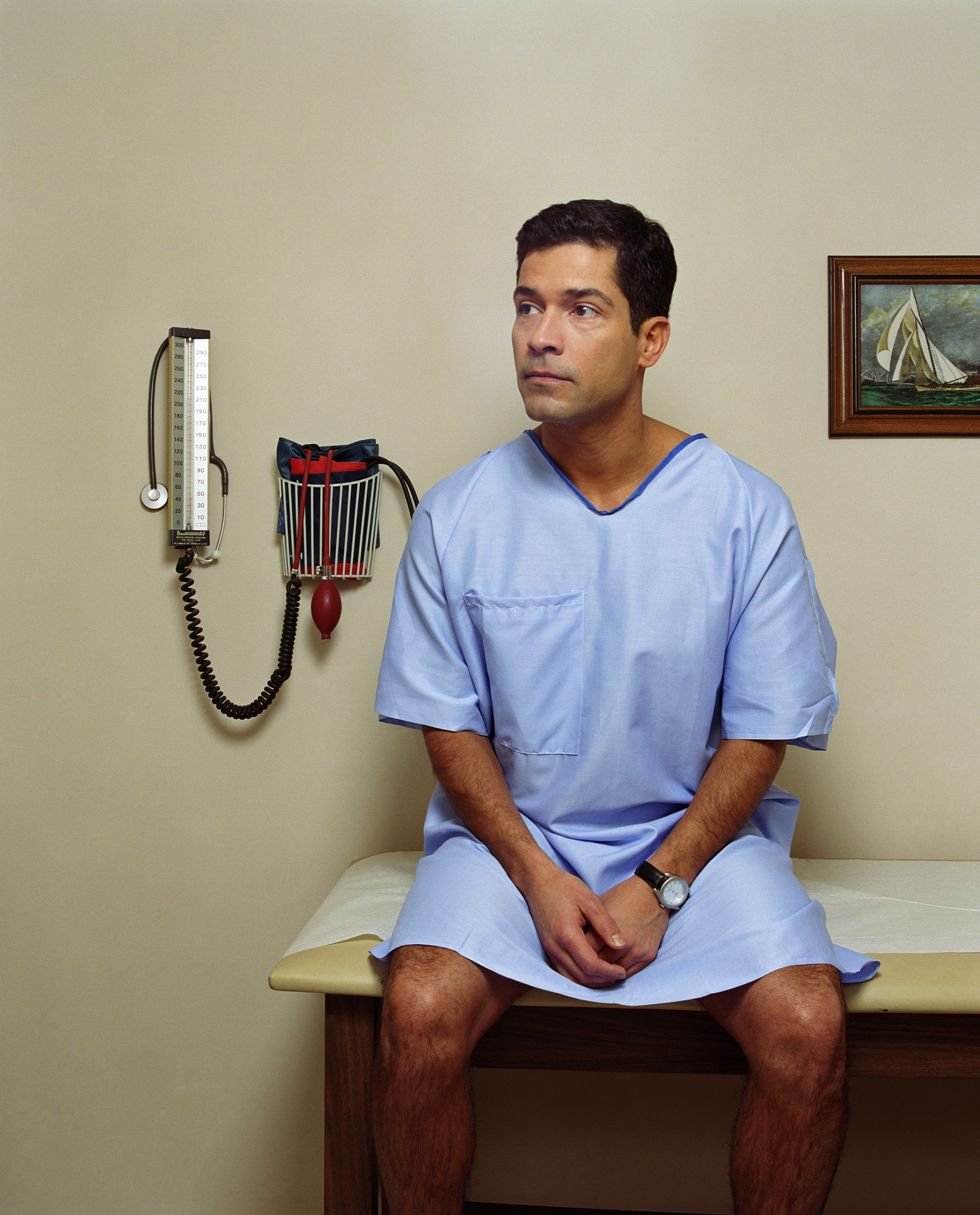 A man in a hospital gown sitting on a doctor&#x27;s office exam table