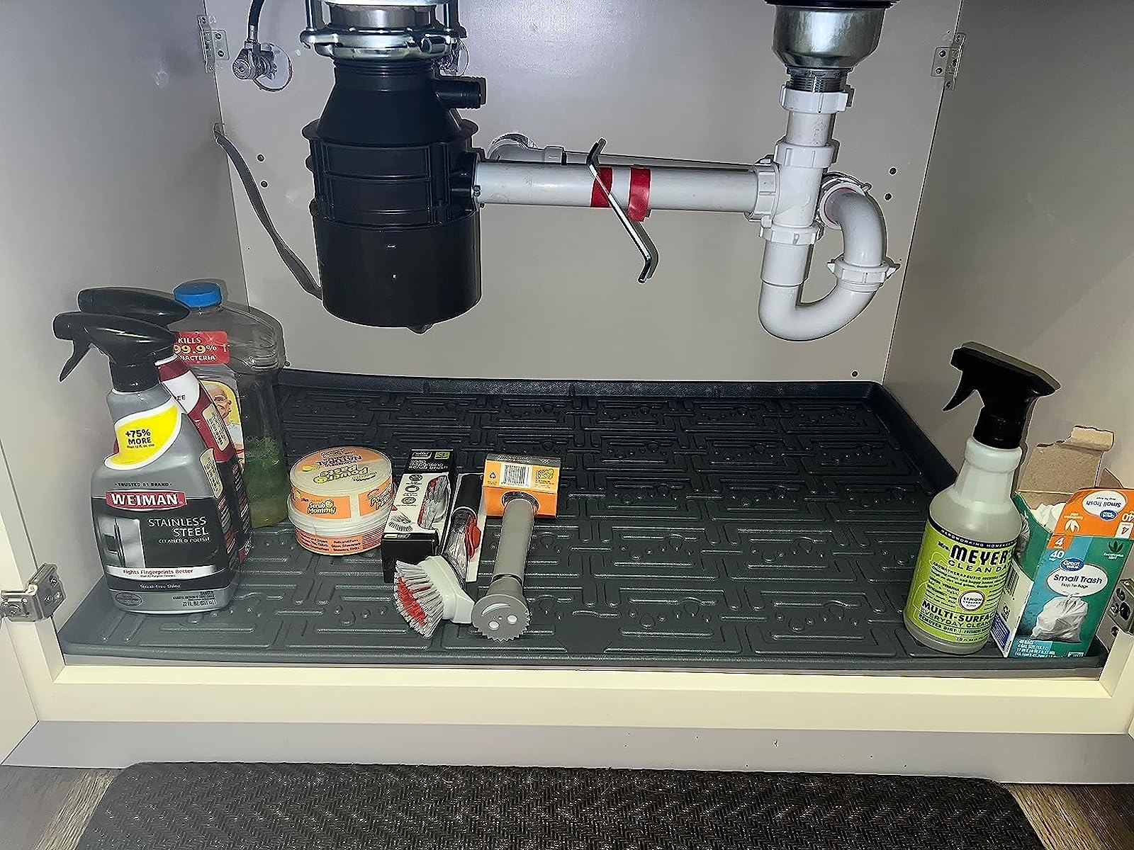 Reviewer image of the black mat lining the bottom of their cabinet with various cleaning supplies on it
