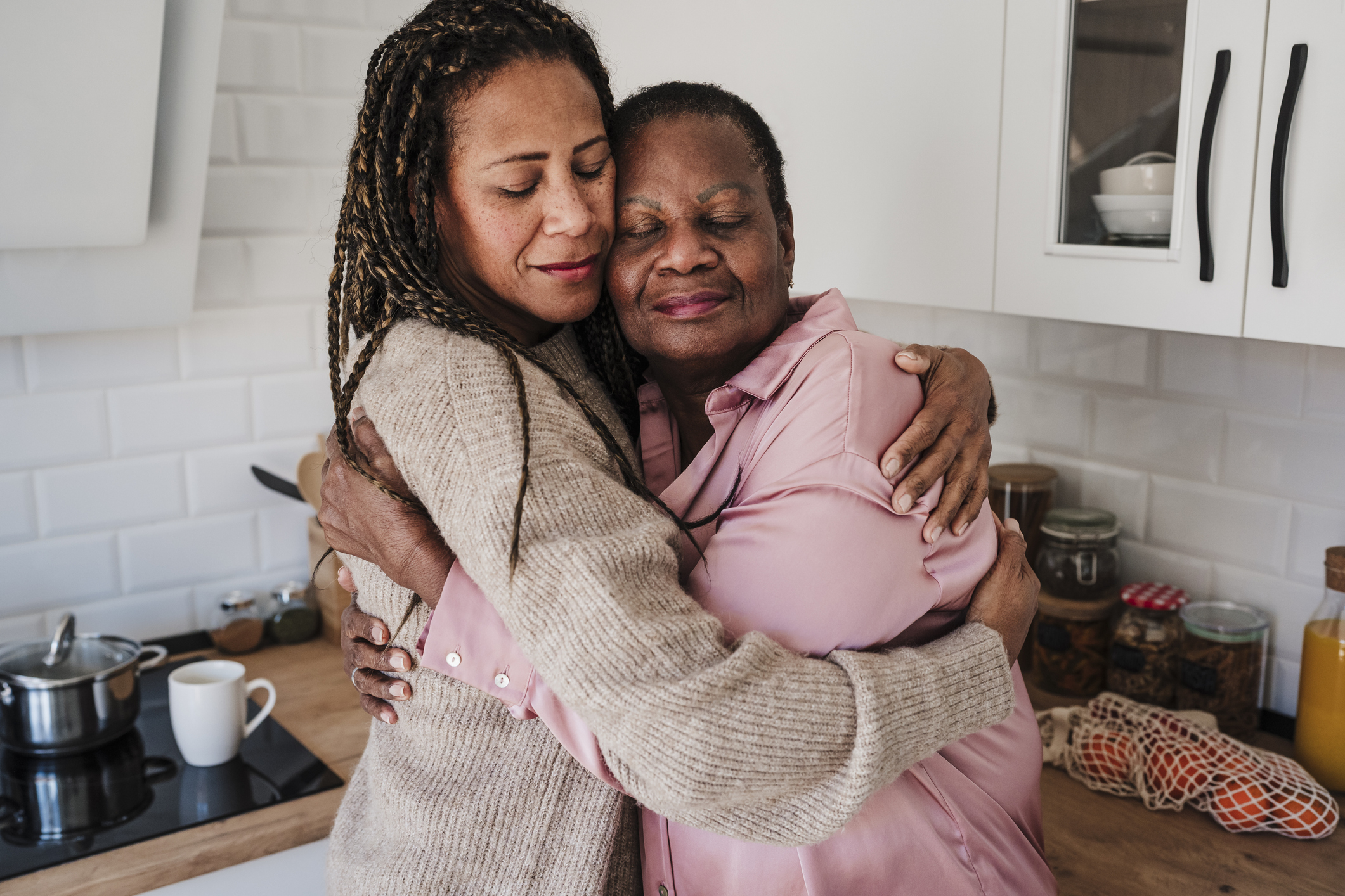 A woman and her mother are hugging in the kitchen