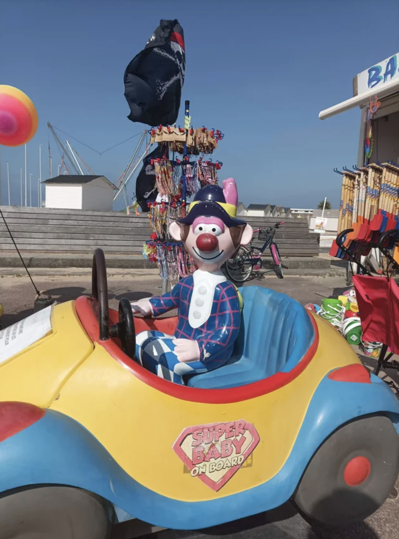 A clown in a creepy two-seater car meant for children to sit in