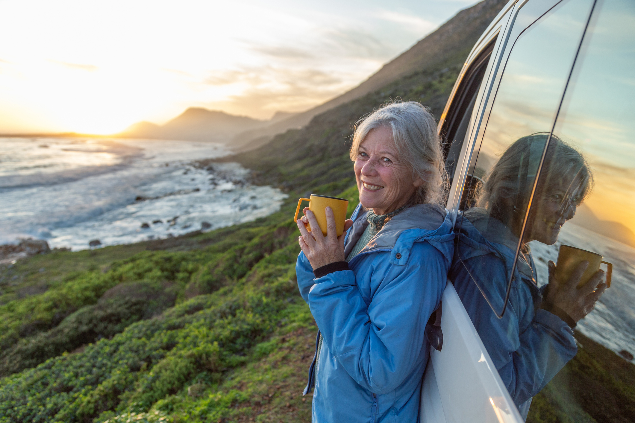 A woman looking out at the ocean and drinking coffee