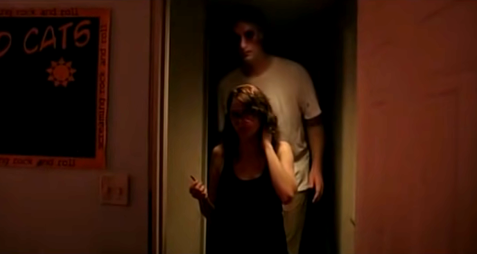 A very tall man following a woman down a dark hallway