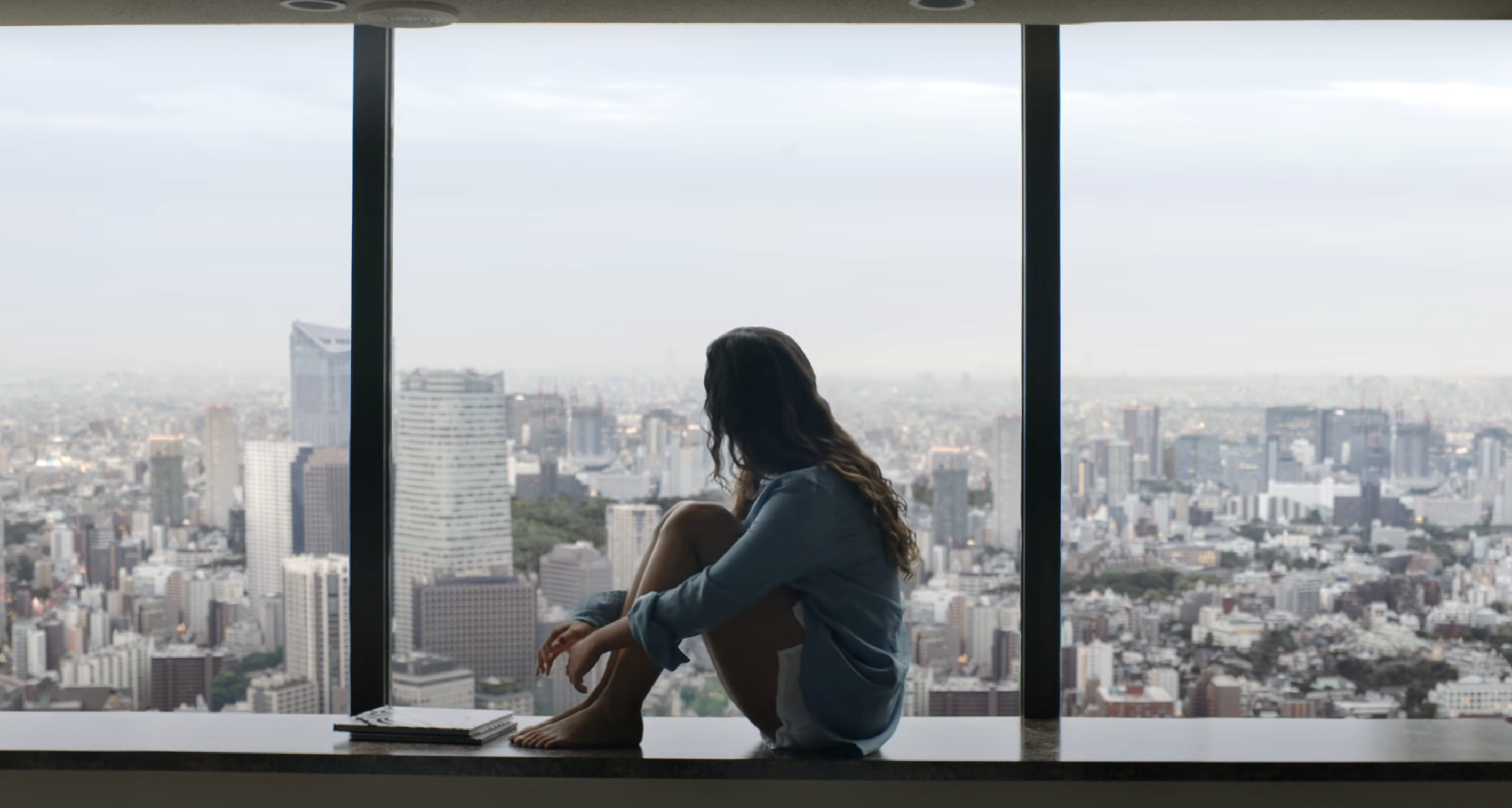 A woman sitting in a hotel window overlooking a city