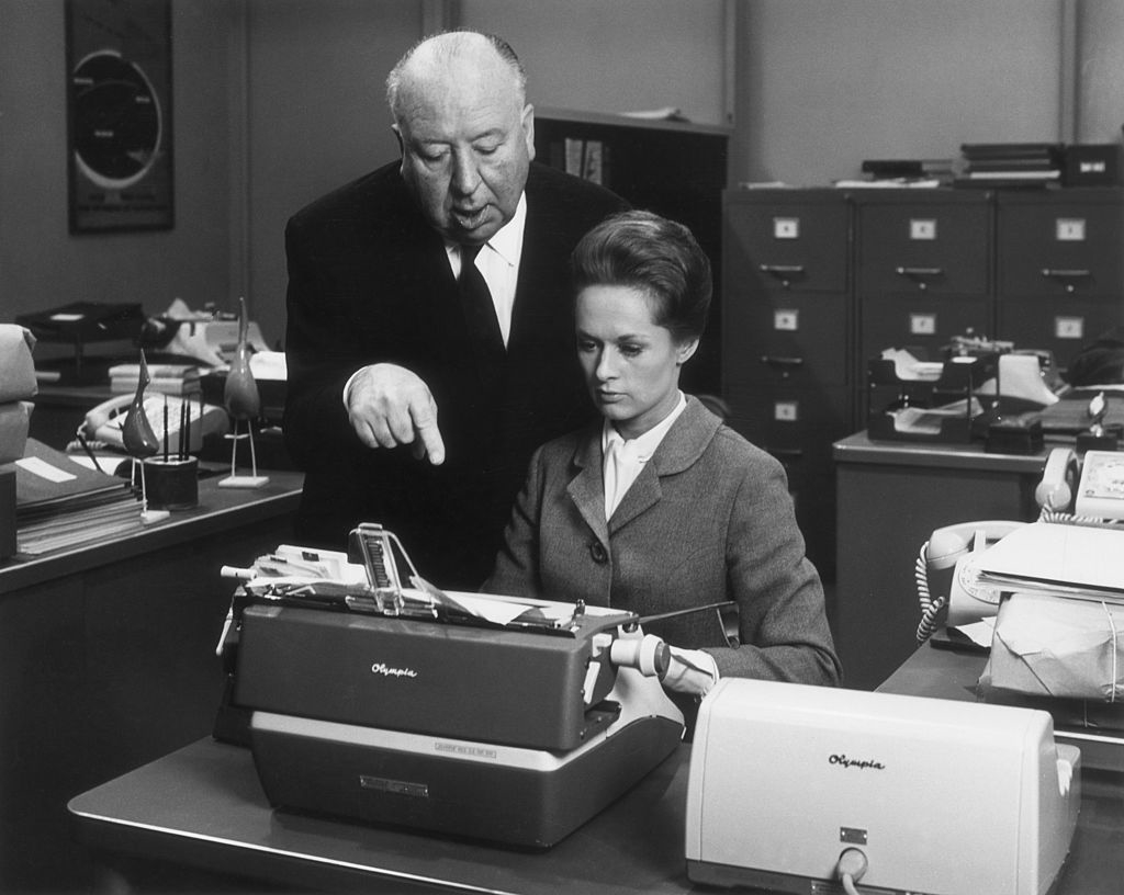 Hitchcock standing behind Hedren, who&#x27;s at a typewriter