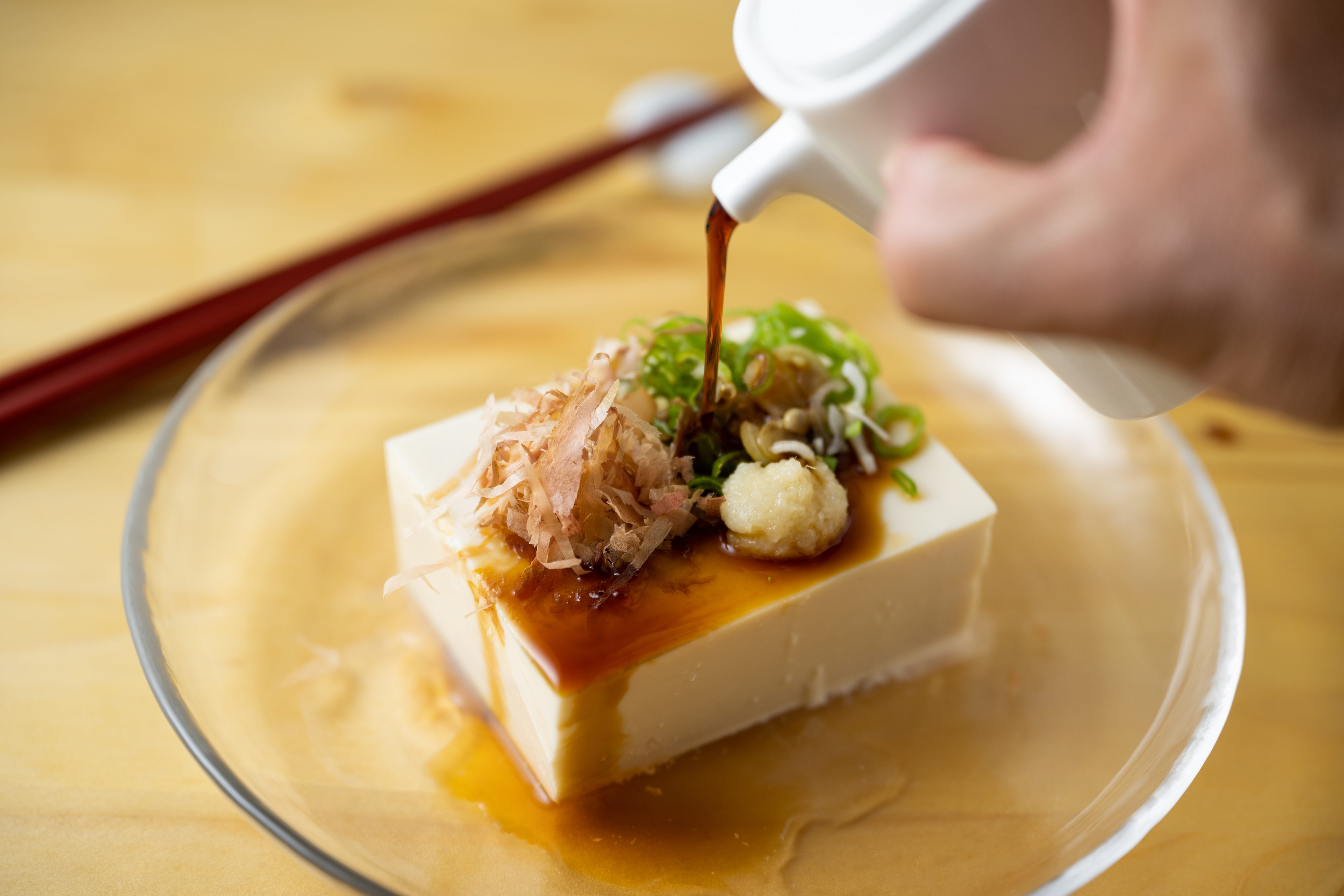 someone pouring soy sauce over a block of tofu