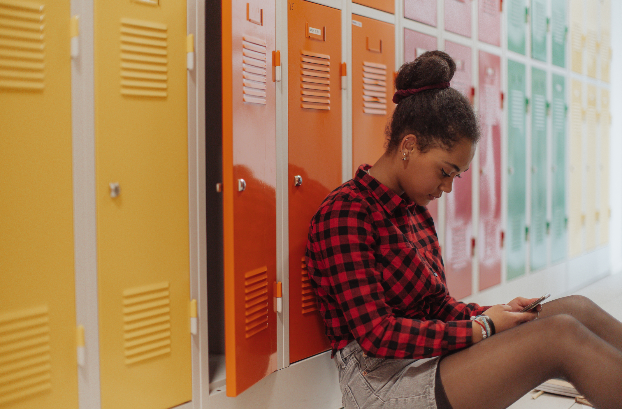 A young girl leaning against a school locker and looking at her phone