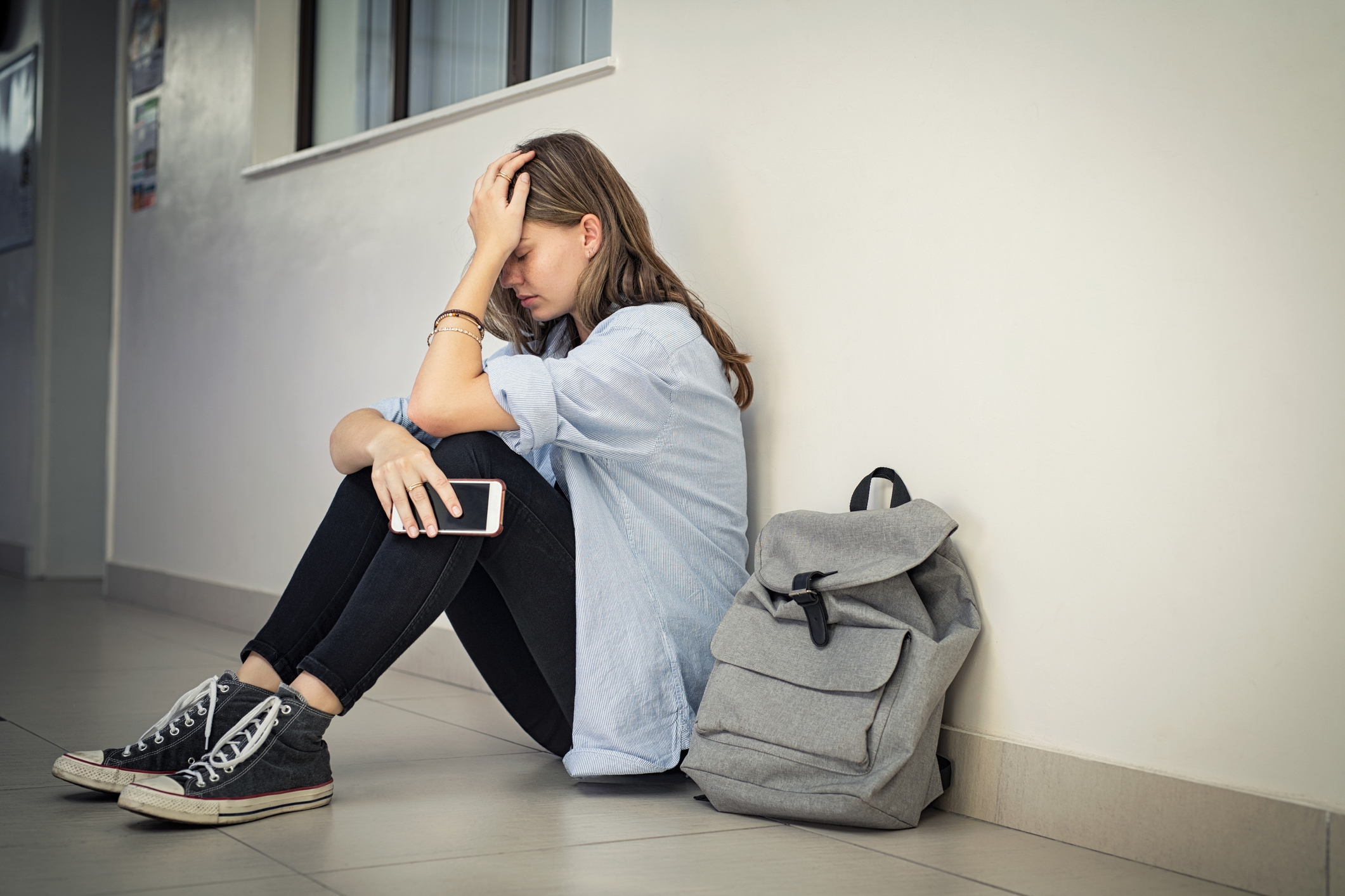 A young girl sitting on the ground next to her backpack crying