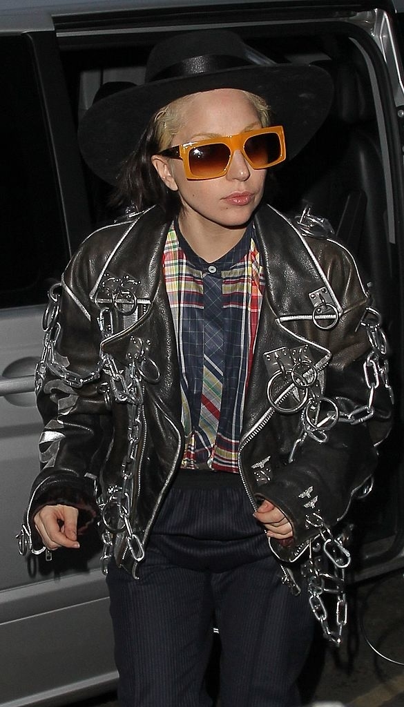 wearing an oversized leather jacket, large sunglasses at night, and a hat