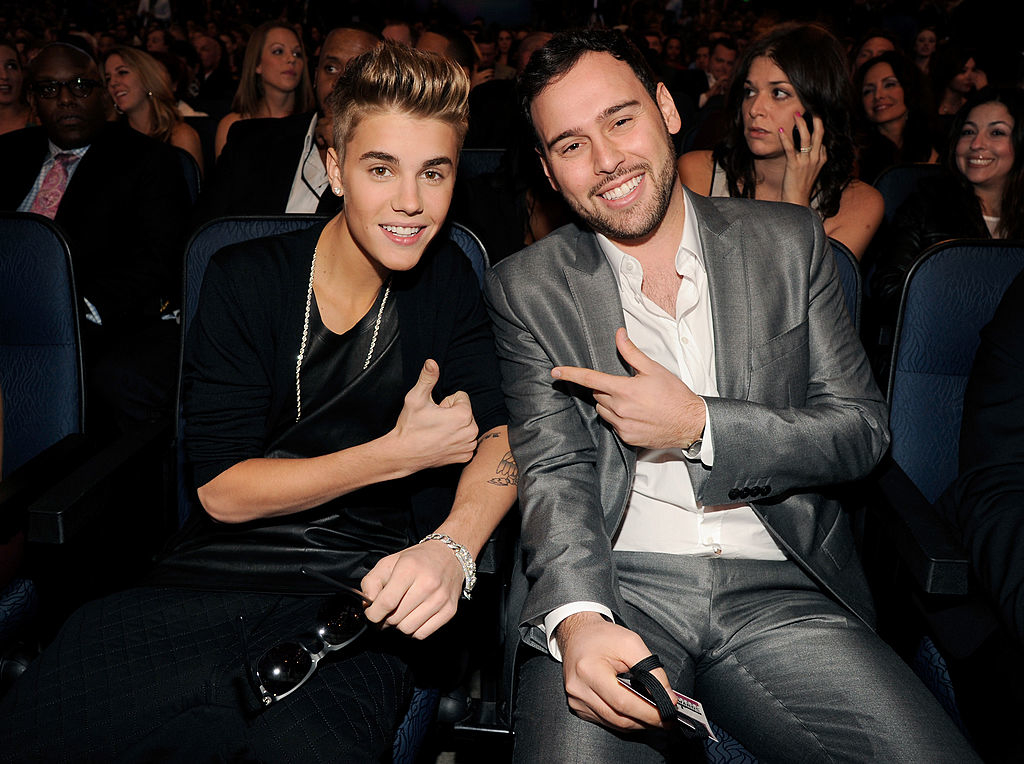 Justin and Scooter sitting together in an audience and smiling