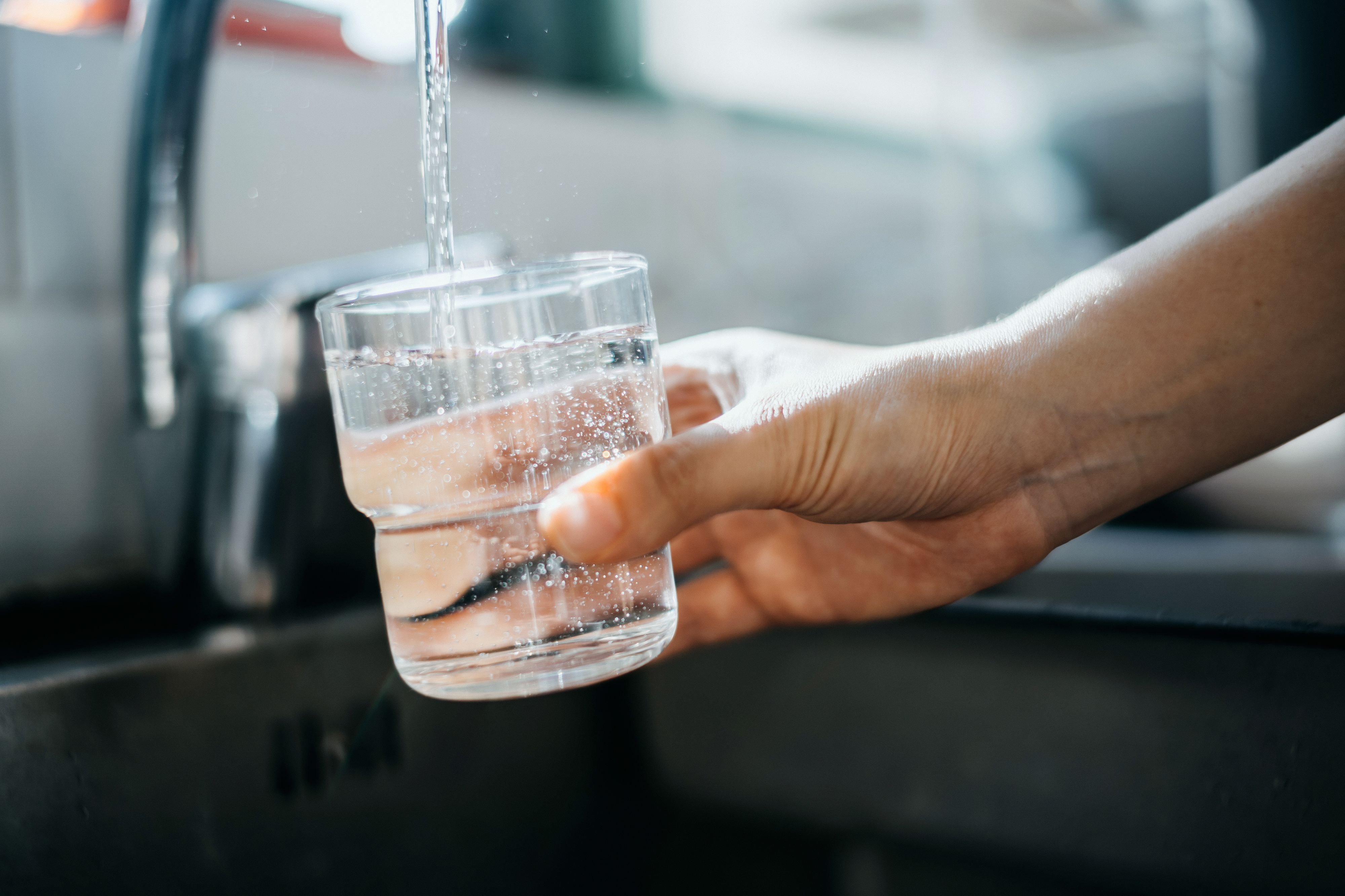 woman filling a glass of water in the sink