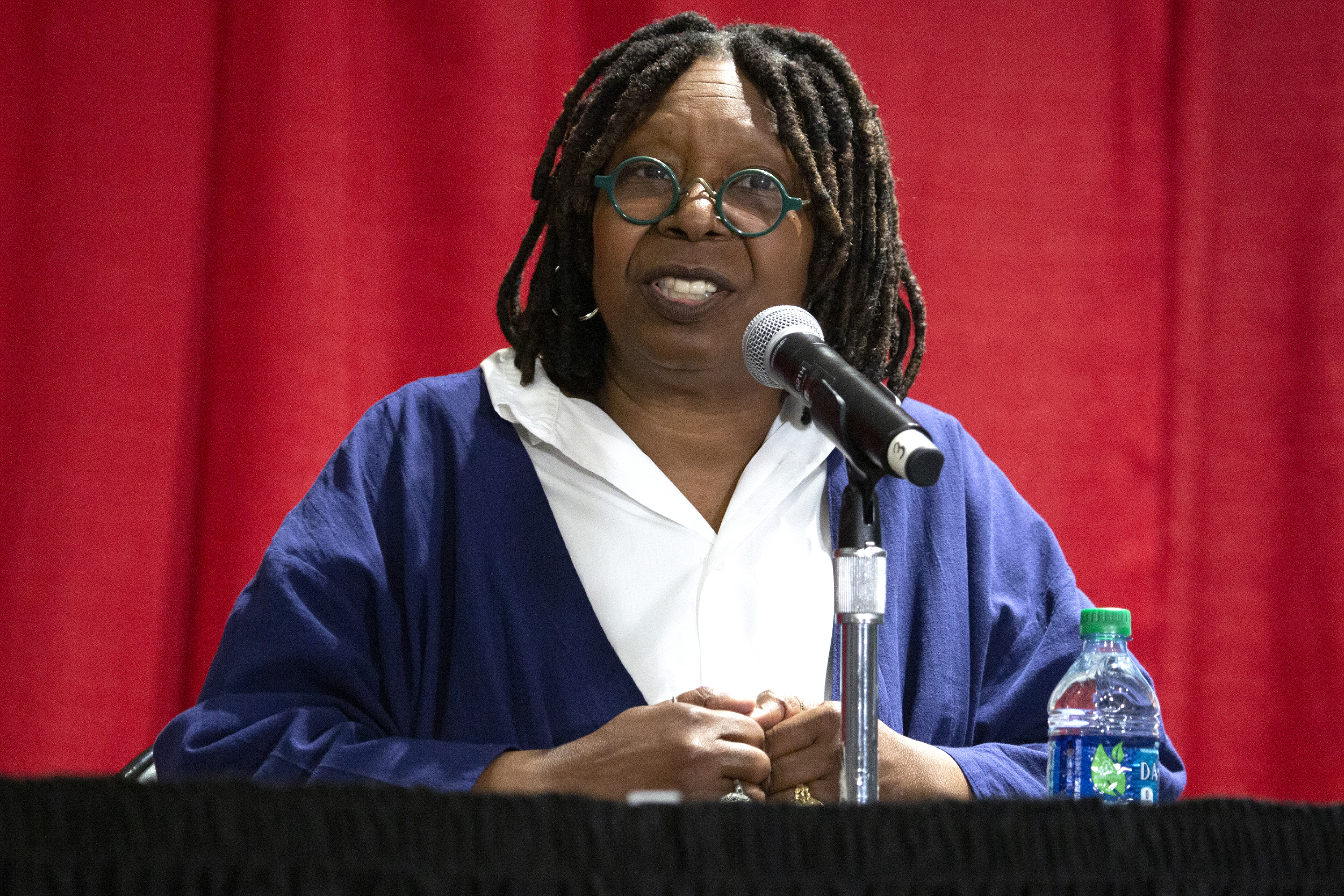Whoopi Goldberg sitting onstage speaking into a microphone