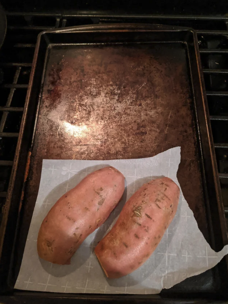 baking sheet with burned on oils and two sweet potatoes