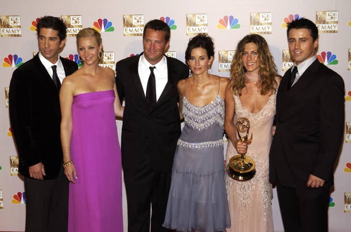 The cast standing together at a media event, with Jennifer Aniston holding an Emmy Award