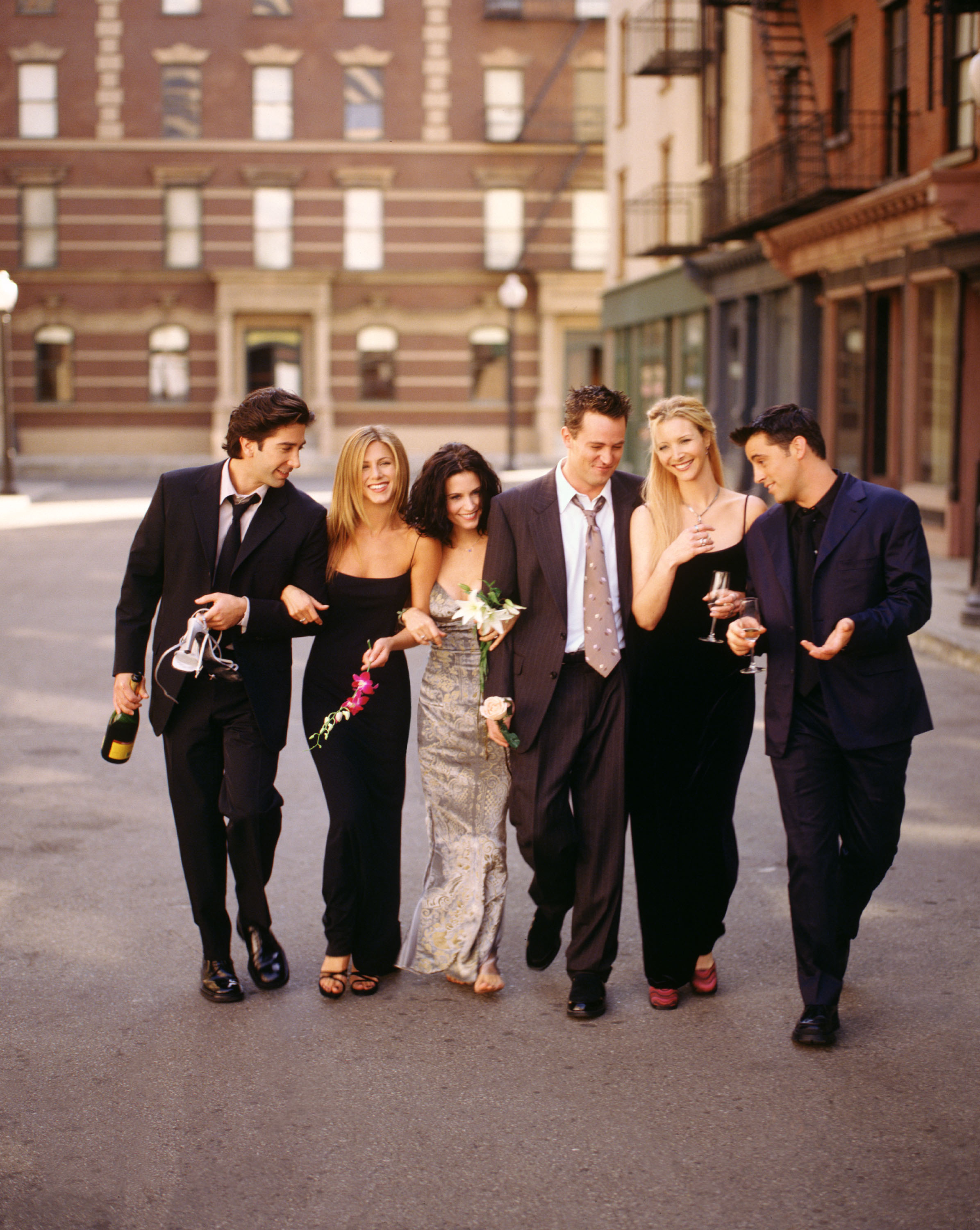 The cast in a scene walking down the street in suits and gowns