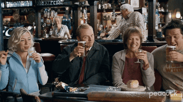 A man with his friends sitting at a booth in the pub making a toast towards the camera