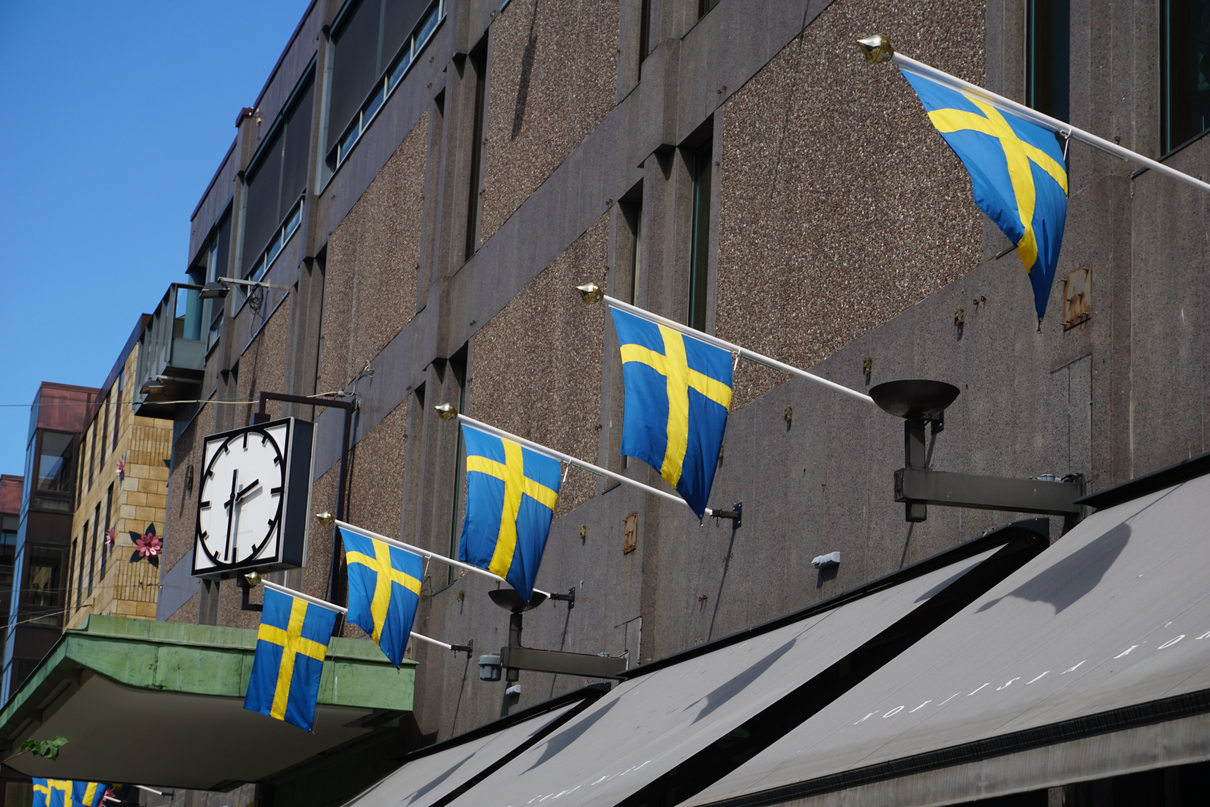 Flags that consist of a yellow or gold Nordic cross on a field of light blue hang from a building exterior