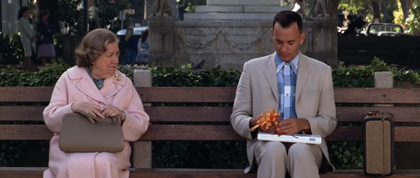Forrest sitting on a bench with an older woman and a box of chocolates
