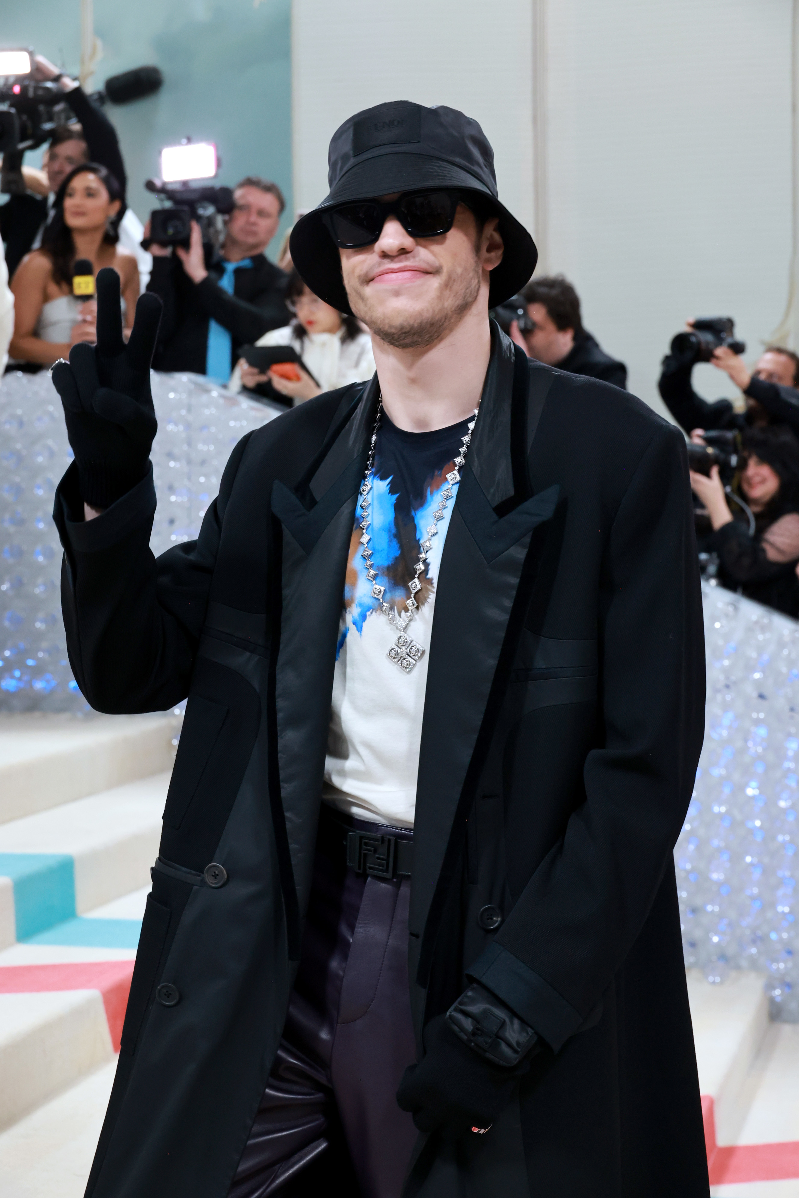 Close-up of Pete at a media event in a long coat, gloves, sunglasses, and hat