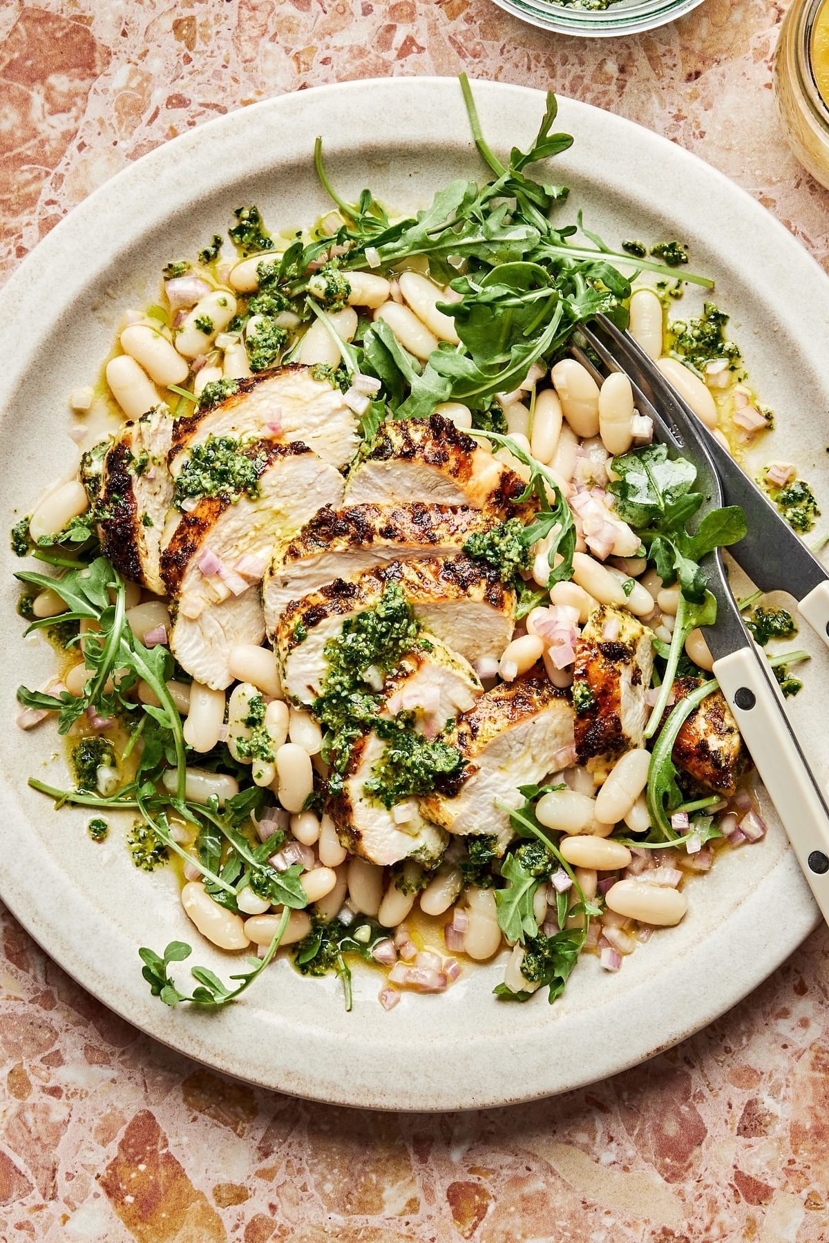 sliced chicken on top of a bed of arugula and white beans