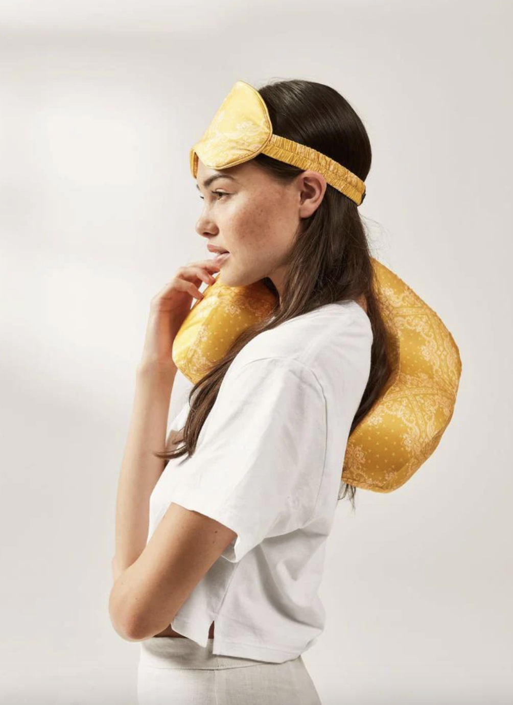 a model using a yellow, bandana-print eye mask and neck pillow