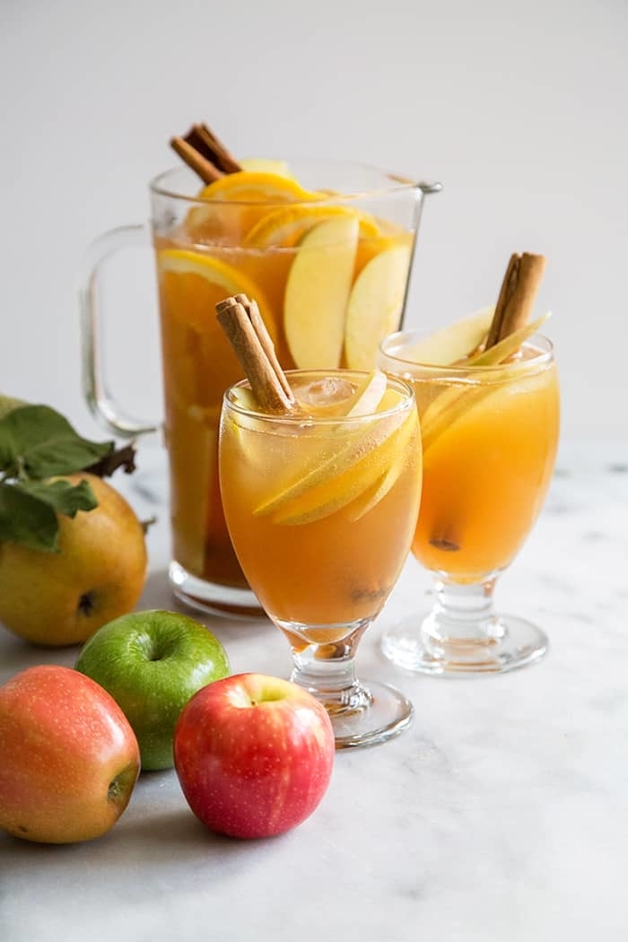 apple punch in a large pitcher and two glasses topped with cinnamon sticks