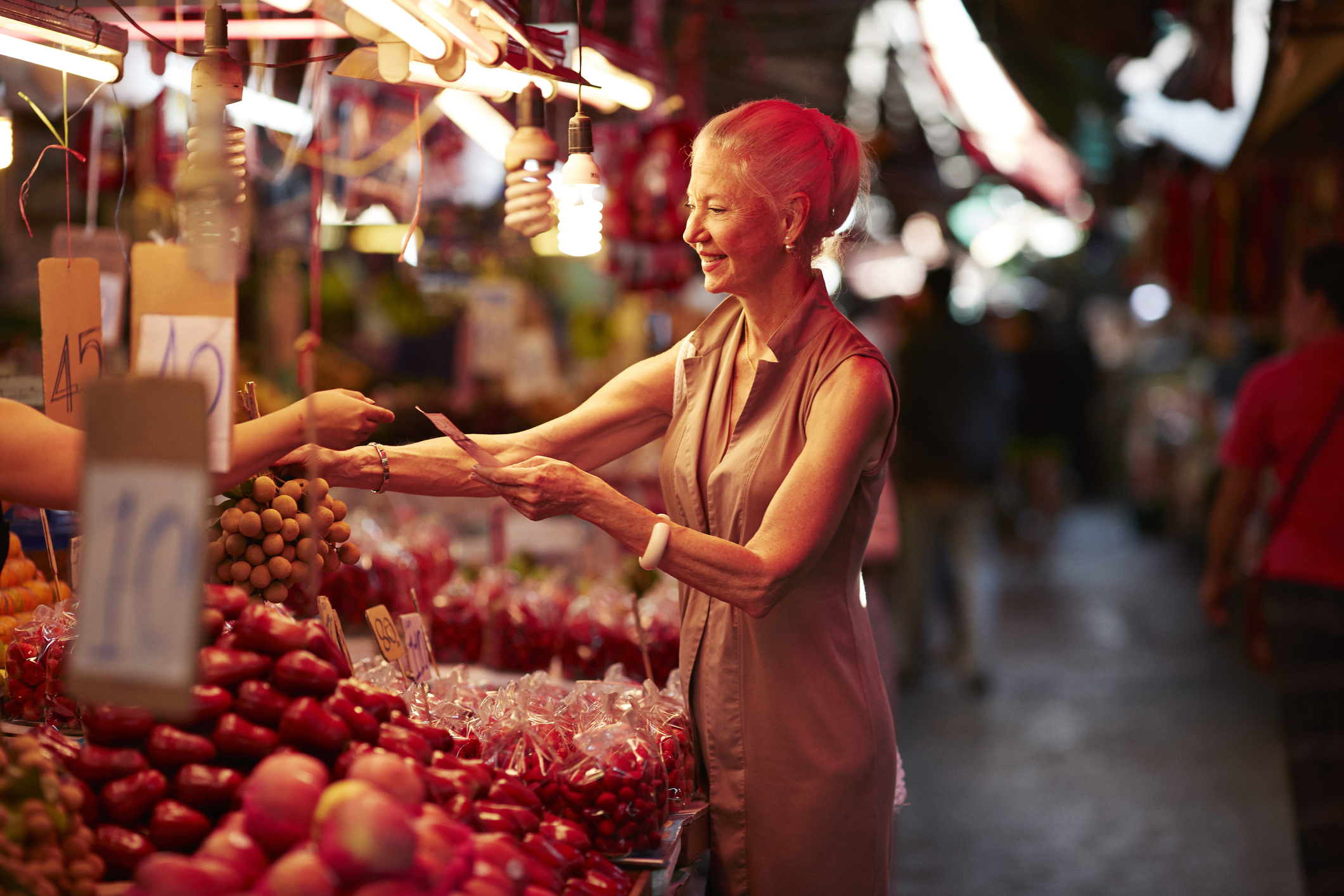 Smiling senior woman paying for langsat fruit while standing at market stall