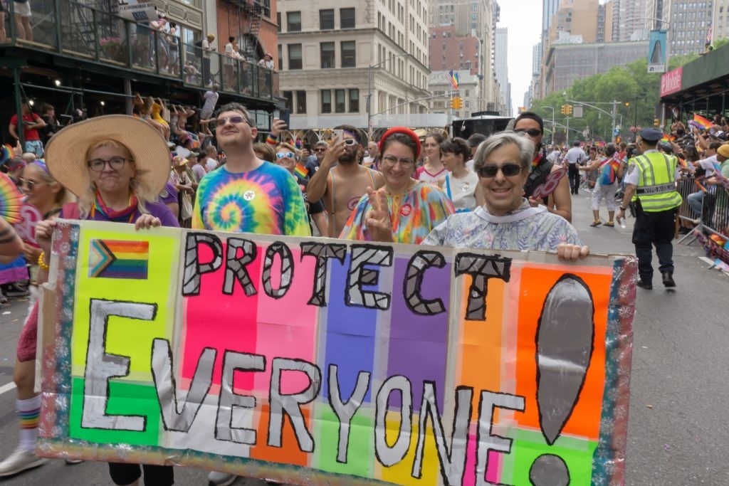 A family at New York Pride is holding up a banner that says &quot;Protect Everyone!&quot;