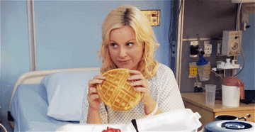Leslie Knope from Parks and Rec eating a waffle in a hospital bed