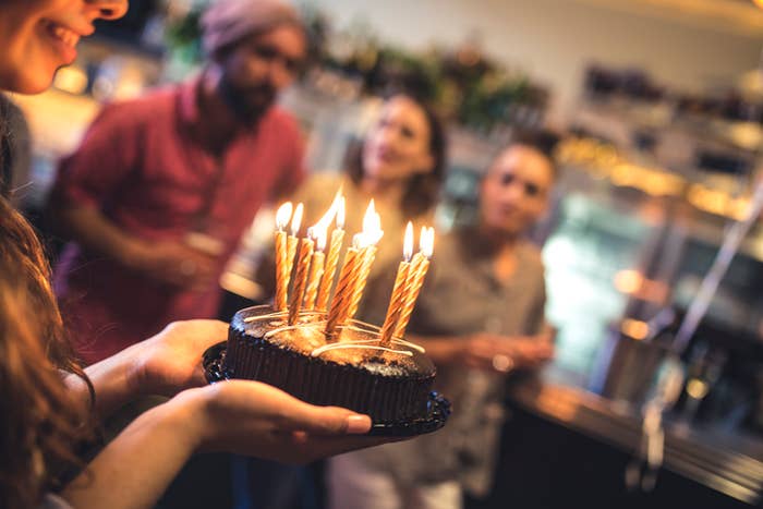 person holding a small cake with lit candles on it
